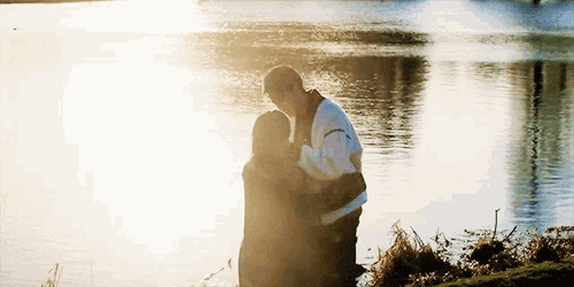 a man and a woman are hugging by a body of water
