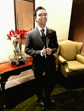 a man in a suit and tie smiles in front of a chair