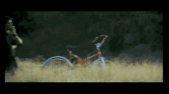 a man smoking a cigarette in a field with a bicycle in the foreground