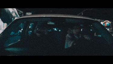 a group of people are sitting in a car at night smoking cigarettes .