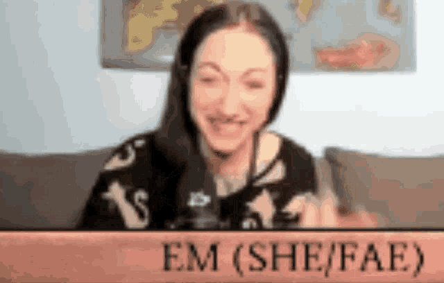 a woman is sitting on a couch with a sign that says em ( she / fae )