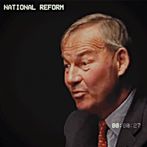 a man in a suit and tie is talking in front of a screen that says " national reform "