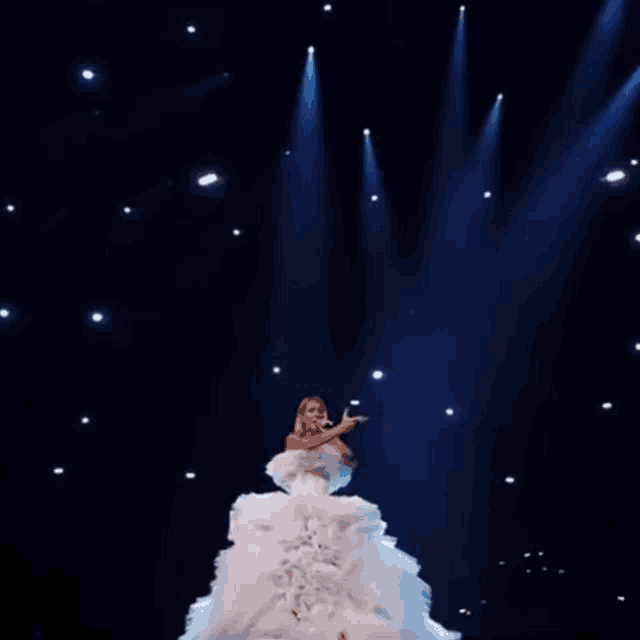 a woman in a white dress sings into a microphone on a stage