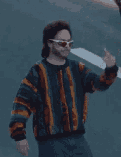 a man in a sweater and sunglasses is giving the middle finger .