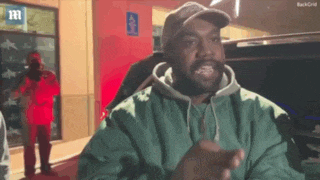 kanye west is wearing a green jacket and a hat while talking to a camera .