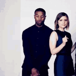 a man in a black shirt and a woman in a blue dress are standing next to each other in a room .