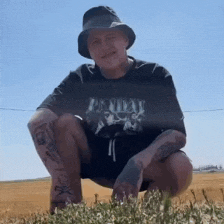 a man wearing a hat and a t-shirt is squatting down in a field .