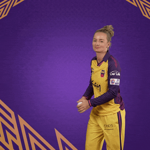 a woman wearing a yellow and purple jersey that says chennai super kings is throwing a ball