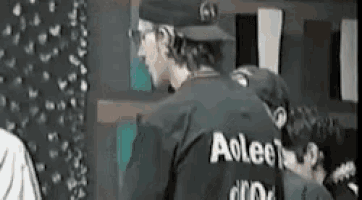 a man wearing a baseball cap and a black shirt with the word aoleon on the back is standing in a room .
