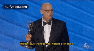 a man in a suit and bow tie is holding a trophy and giving a speech .