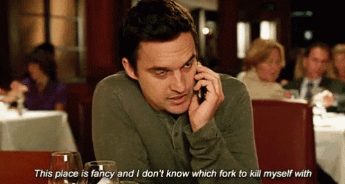 a man is talking on a cell phone in a restaurant while sitting at a table with wine glasses .