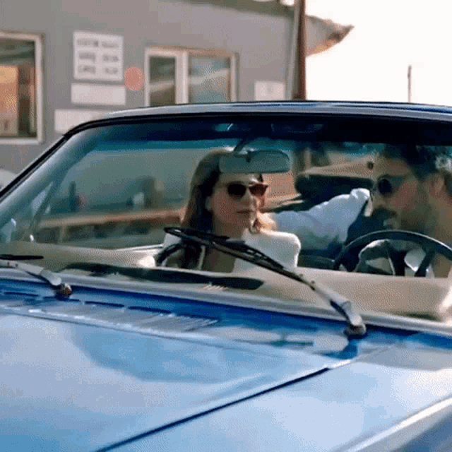 a man and a woman are sitting in a blue convertible car .