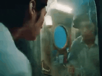 a man is looking out of a plane window at another man .