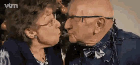 an elderly couple kissing in front of a christmas tree