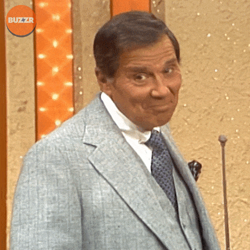a man in a suit and tie stands in front of a microphone with buzzr written in the corner