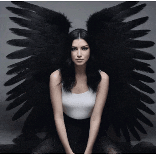 a woman with black angel wings is sitting down with her legs crossed