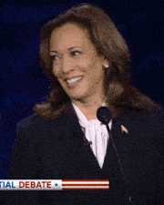 a woman is giving a speech in front of a sign that says ' debate ' on it