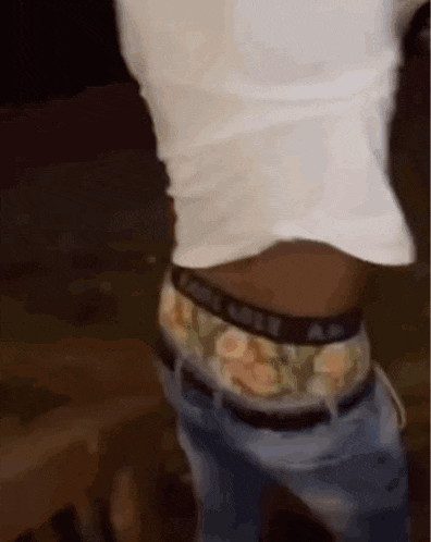 a man in a white shirt and camouflage underwear is standing in the dark .