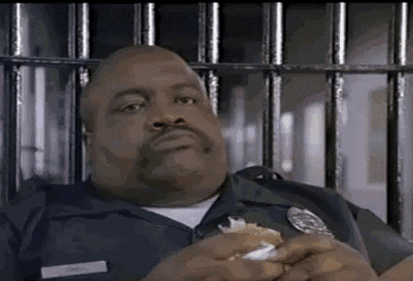 a police officer is sitting in a jail cell eating a sandwich .