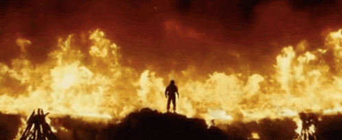 a silhouette of a man standing on top of a burning hill