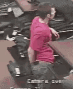 a man in a red shirt is sitting at a desk in front of a camera that says camera over