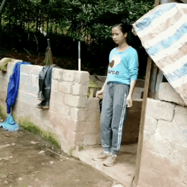 a girl wearing a blue shirt that says since is standing outside of a building