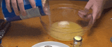 a person pouring liquid into a glass bowl