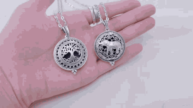 a person is holding a tree of life and elephant necklace