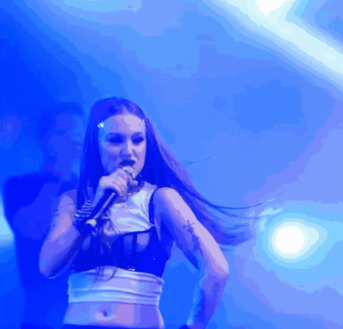 a woman singing into a microphone with a blue light behind her