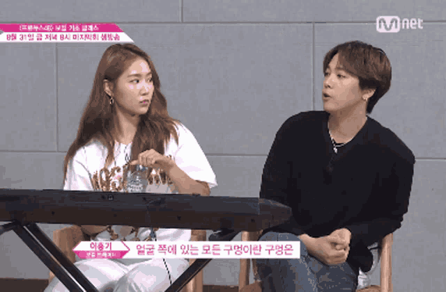 a man and a woman are sitting next to each other in front of a keyboard and a sign that says mnet on it