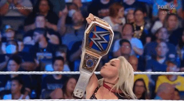 a woman in a wrestling ring is holding a championship belt and kissing it .