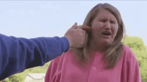 a woman in a pink sweater is being punched in the face by a man in a blue sweater .