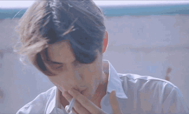 a man in a white shirt is smoking a cigarette with his eyes closed .