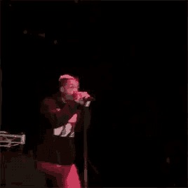 a man is singing into a microphone on a stage in the dark .