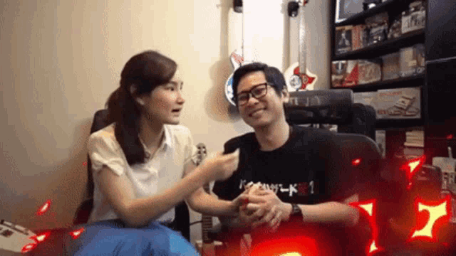 a man and a woman are sitting next to each other and the man is wearing a black shirt that says ' k '