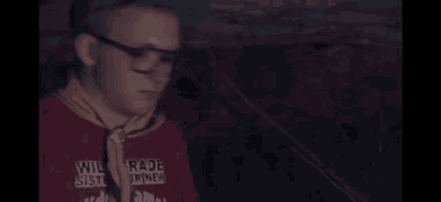 a man wearing glasses and a hat is standing in the dark .