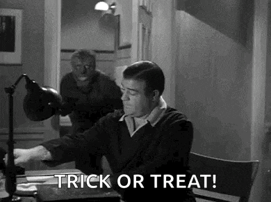 a man is sitting at a desk in front of a lamp while a werewolf appears in the background .