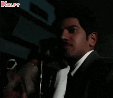 a man in a suit and tie is standing in a dark room with a kulfy logo in the corner .