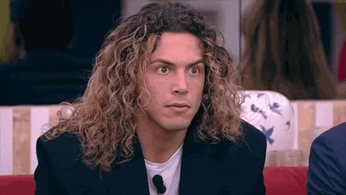a man with long curly hair is sitting on a couch looking at the camera .