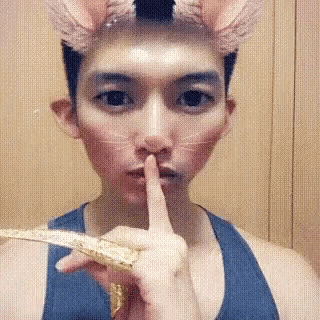 a man with a cat mask on his face is holding his finger to his mouth .