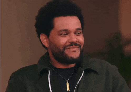 a man with a beard wearing a green jacket and a necklace is smiling .
