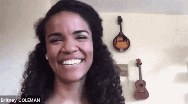 britney coleman is smiling in front of a wall with guitars hanging on it