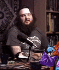 a man with a beard is sitting at a table with a microphone .