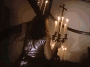a woman is standing in a dark room with candles and a cross on the wall .