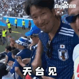 a man wearing a blue shirt with a japanese flag on it is sitting in the stands at a soccer game .