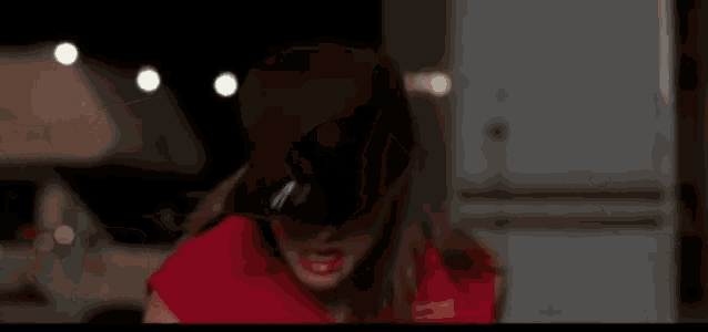 a woman in a red shirt and a black hat is making a funny face .