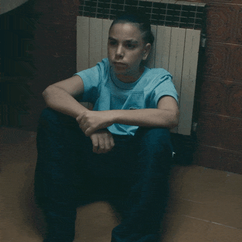 a woman in a blue shirt sits on the floor with her head down