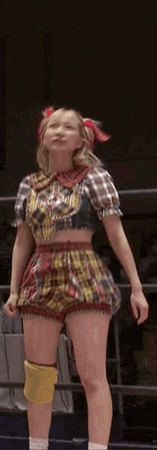 a woman is standing in a wrestling ring wearing a plaid dress and knee pads .