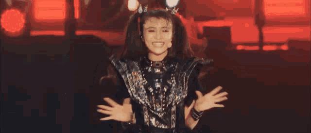 a woman is standing on a stage with her hands in the air and a crown on her head .