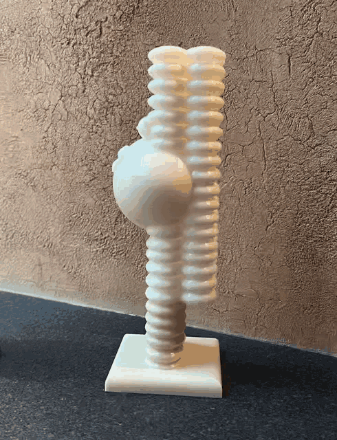 a white sculpture is sitting on a black table in front of a wall